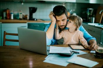 Is Debt Threatening to Ruin Your Retirement Before It Gets Started? 4 Tricks That May Help: https://g.foolcdn.com/editorial/images/684313/stressed-person-looking-at-laptop-and-documents-with-young-child-sitting-on-lap-kissing-their-face.jpg